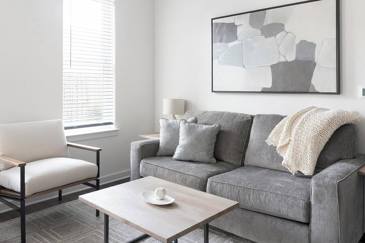 Una sala de estar moderna con un sofá gris, una mesita y una ventana con persianas.