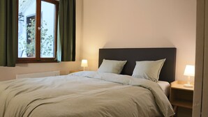 A neatly made bed with a headboard, two bedside lamps, a window with curtains, and a small bedside table. - Modern apartment for 2-4 guests with balcony (Bruttig-Fankel)