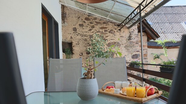 A glass table with a tray of breakfast items, a potted plant, and a view of a stone building. - Modern apartment for 2-4 guests with balcony (Bruttig-Fankel)