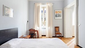 Ett sovrum med en säng, två stolar, ett skrivbord, ett fönster med gardiner och en dörr.