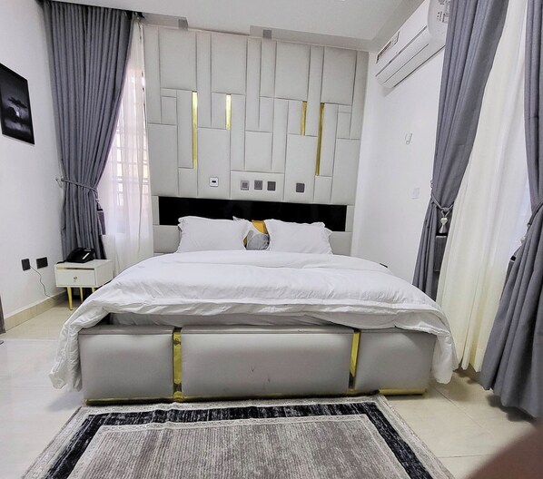 A modern bedroom with a bed, curtains, a bedside table, and a wall-mounted air conditioner. - Times Square Hotel And Suites (Oru)