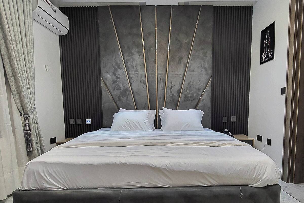 A modern bedroom with a large bed, dark curtains, an air conditioning unit, and a ceiling light fixture.