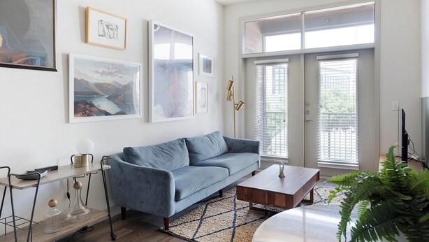 Ein Wohnzimmer mit einem blauen Sofa, einem Couchtisch und einem großen Fenster mit Jalousien.