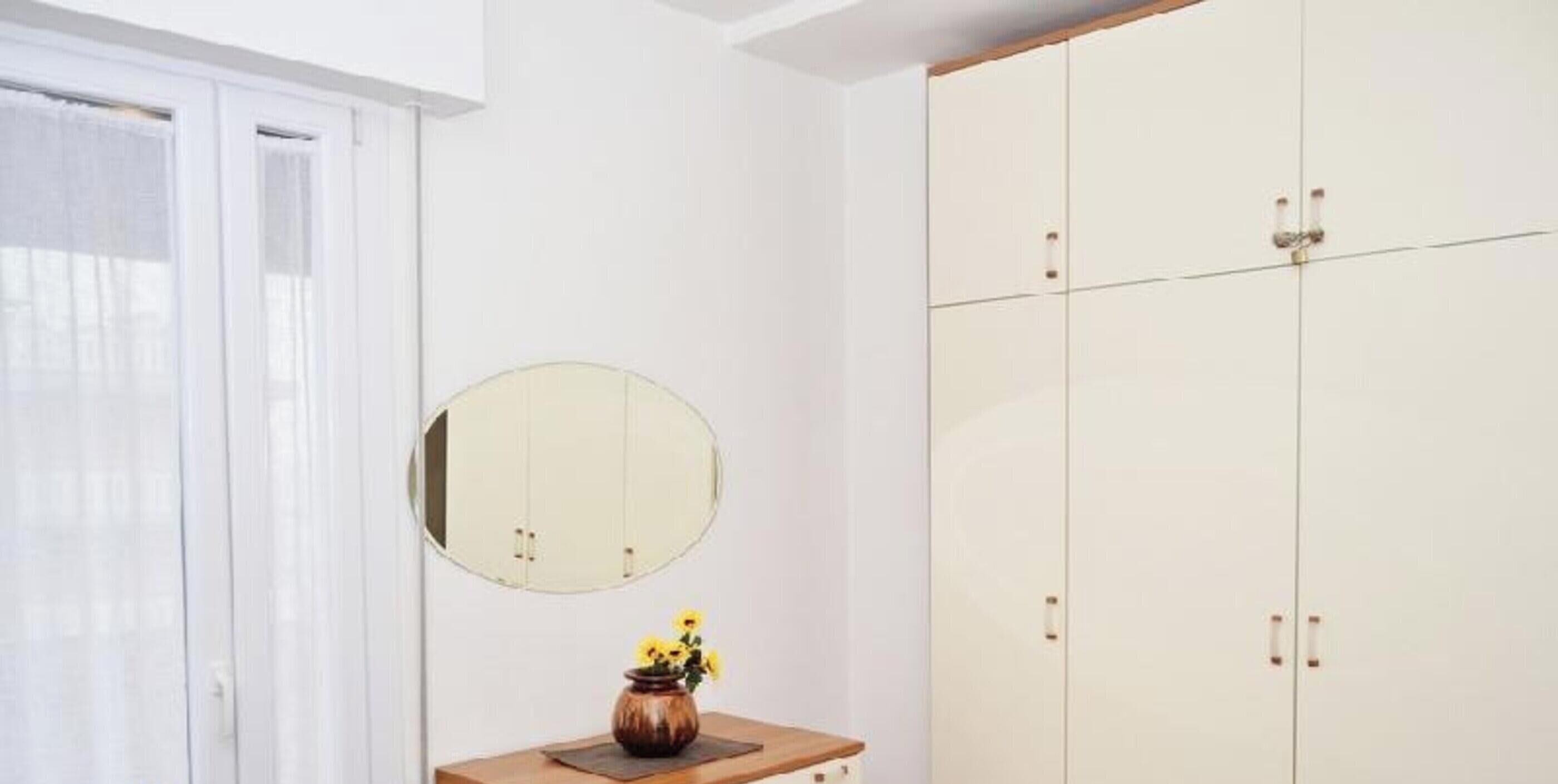 A room with a large wardrobe, a round mirror, and a small table with a vase.
