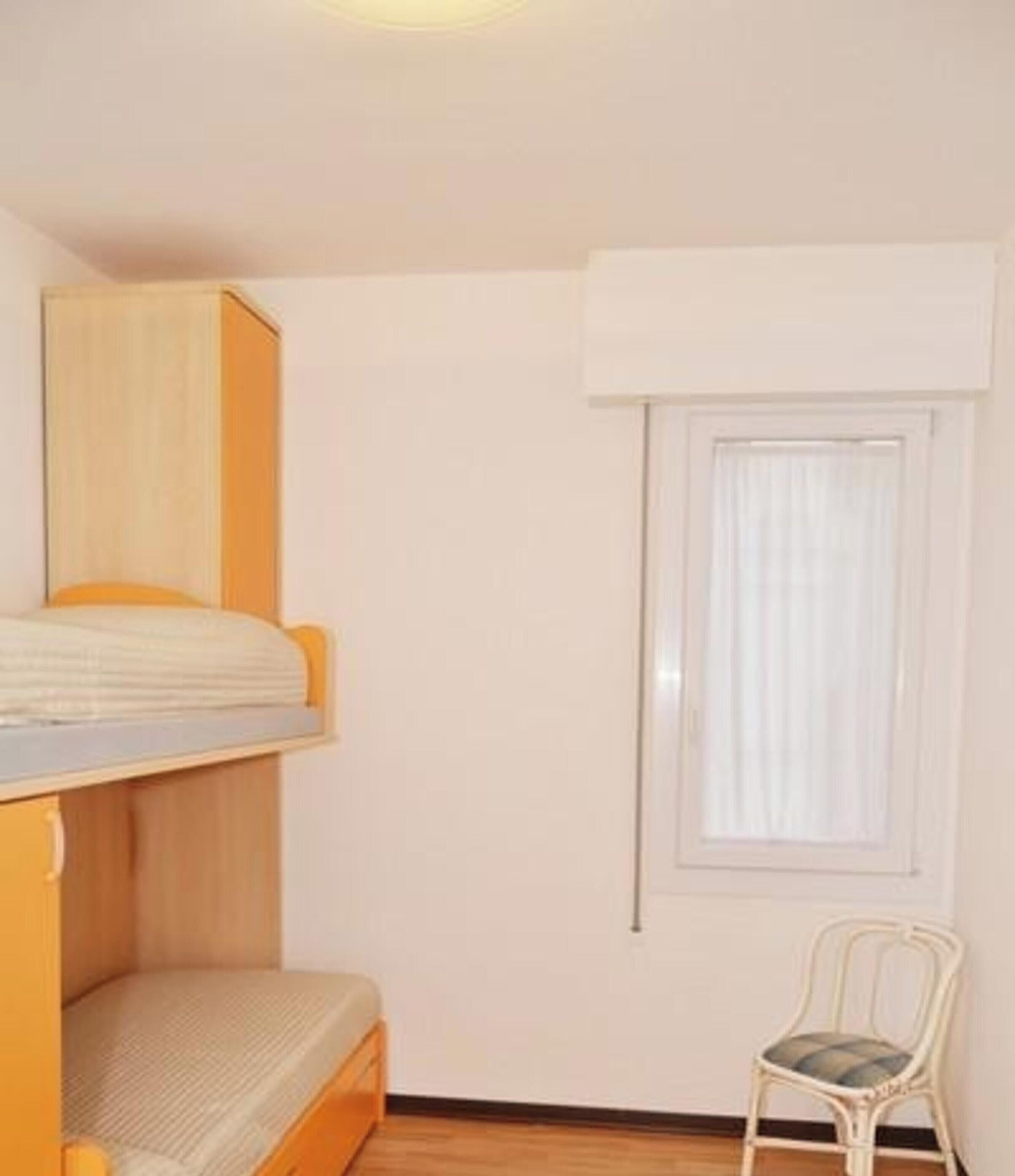 A small room with a bunk bed, a single chair, and a window with curtains.