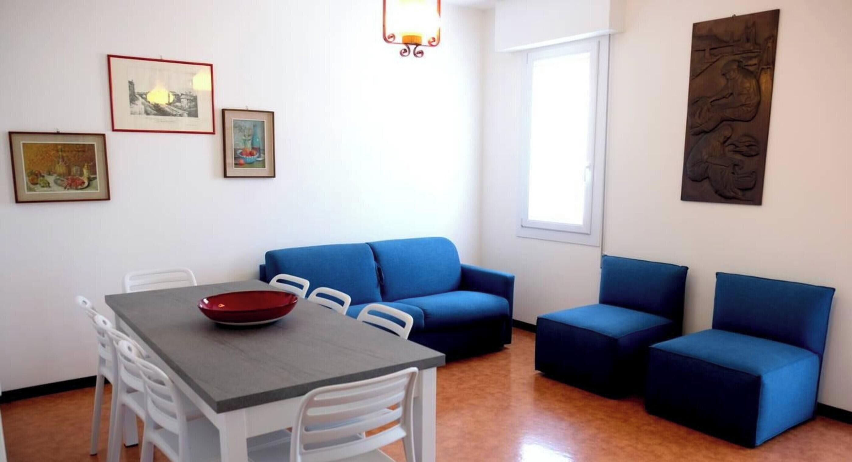 A dining area with a table and chairs, a blue sofa, and a wall with framed pictures.