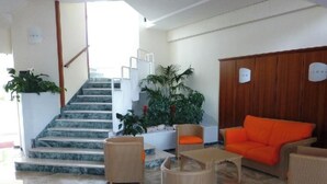 Rebedor d'hotel amb escala, mobles de vimbles, un armari de fusta i plantes en testos.