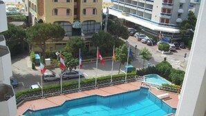 Zona de piscina amb diverses banderes, carretera amb cotxes i edificis circumdants.