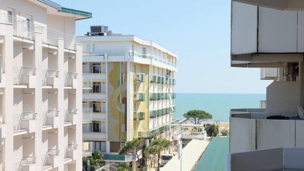 Un edifici de diversos pisos amb balcons, vista al mar i cel blau.