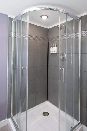 Une cabine de douche fermée par des parois en verre, dotée d’un sol carrelé, d’un pommeau de douche et d’une barre d’appui.