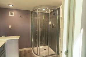 A corner shower with a glass enclosure, a white countertop, and a wall-mounted towel rack. - Greystone (Anderson)