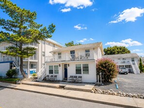 Ein zweistöckiges Motel mit einem Balkon im zweiten Stock, einer kleinen Veranda mit Stühlen und einem Parkplatz davor.
