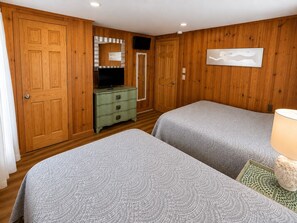 Ein Zimmer mit zwei Betten, Holzwänden, einem Schminktisch, einem Fernseher und einer Lampe.