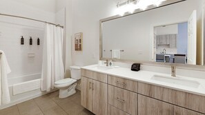 A modern bathroom with a bathtub, toilet, and vanity with a large mirror. - Landing Apartments Fort Worth Near Historic Southside (Fort Worth)