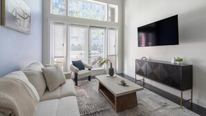 Ein modernes Wohnzimmer mit Sofa, Sessel, Couchtisch und einem an der Wand befestigten Fernseher.