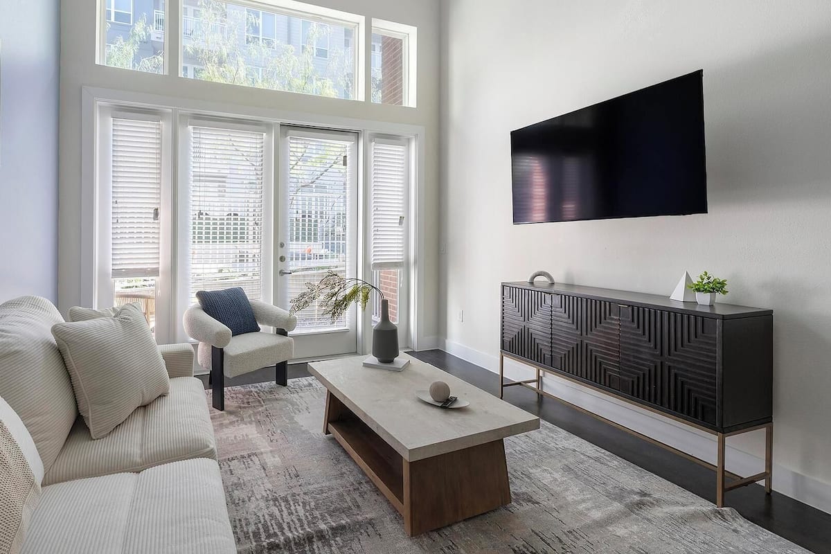 A modern living room with a sofa, armchair, coffee table, and a TV mounted on the wall.