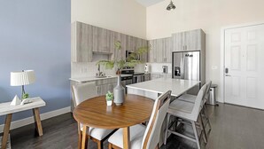 Eine moderne Küche mit grauen Schränken, einem Edelstahlkühlschrank und einem Essbereich mit einem Holztisch und grauen Stühlen.