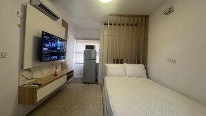 A hotel room with a bed, a TV mounted on a wall, a small kitchenette, and a sliding door. - Cozy 1-bedroom apartment in peaceful Lagos with AC, gym and pool access (Lagos)