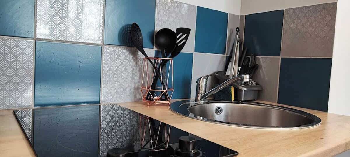 Een keuken met een roestvrijstalen spoelbak, een zwart inductiefornuis en een koperen keukengerei-houder.