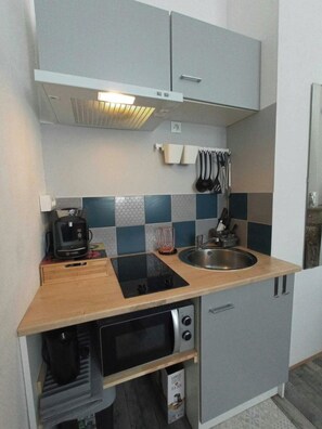 Una kitchenette compacta con microondas, horno y pileta integrados, destacando un salpicadero de baldosas a cuadros y una encimera de madera.