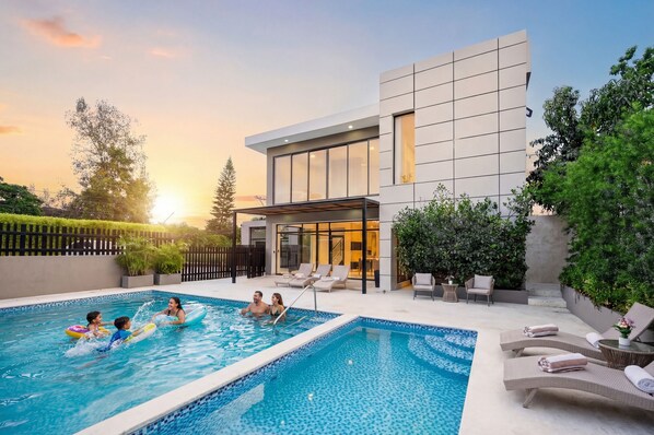 A modern house with a swimming pool, outdoor seating, and a large glass door.