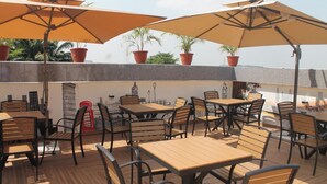 Eine Dachterrasse mit Holztischen und -stühlen, Blumentöpfen und großen Sonnenschirmen.
