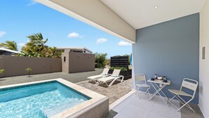 Ett modernt utomhusområde med pool, bubbelpool, solstolar och ett bord med drycker.