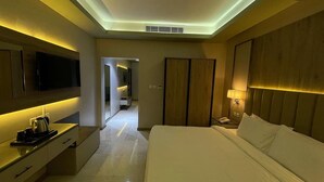 A modern hotel room with a flat-screen TV, a bedside table with a lamp, a large bed, and a wardrobe.