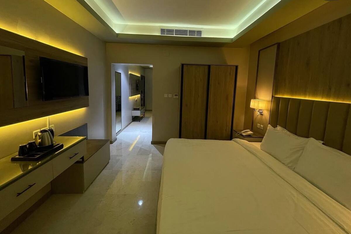 Una habitación de hotel moderna con televisión de pantalla plana, una mesita de noche con lámpara, una cama grande y un armario.