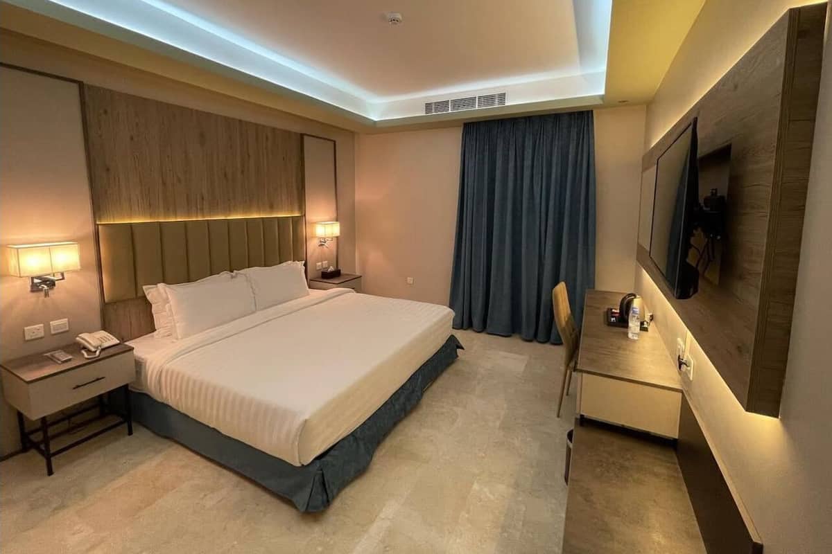Habitación de hotel con una cama grande, mesitas de noche con lámparas, un escritorio y un televisor de pantalla plana montado en la pared.