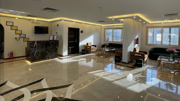 A spacious lobby with a marble reception desk, comfortable seating, large windows, and a fire extinguisher.