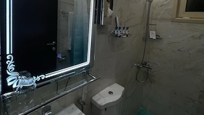 A bathroom with a large mirror, a handheld showerhead, a toilet, and a sink.