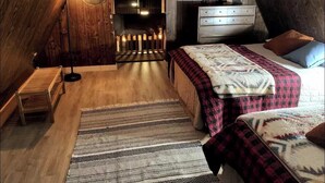 Une chambre de style « loft », avec un plafond en pente, un plancher en bois, un lit avec une literie à motifs, une commode et une table de chevet.