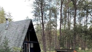Une cabane avec un toit en pente, une terrasse en bois et un foyer entouré de bûches.