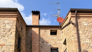 Il s’agit d’un bâtiment en pierre doté d’une cheminée, d’une antenne parabolique et d’une petite fenêtre. On y voit deux chaises blanches et une table à l’extérieur.