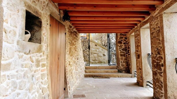 Un couloir en pierre, avec des poutres en bois, d’où l’on peut admirer le paysage extérieur.