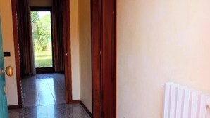 Un pasillo con una puerta que da a una habitación, un radiador en la pared y vistas a zonas verdes afuera.