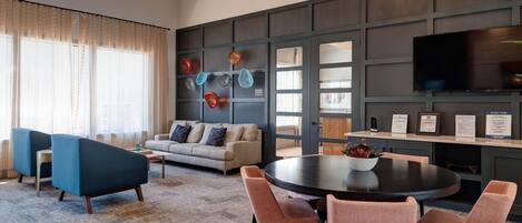 A modern hotel room with a sofa, chairs, a round table, and a TV mounted on the wall.