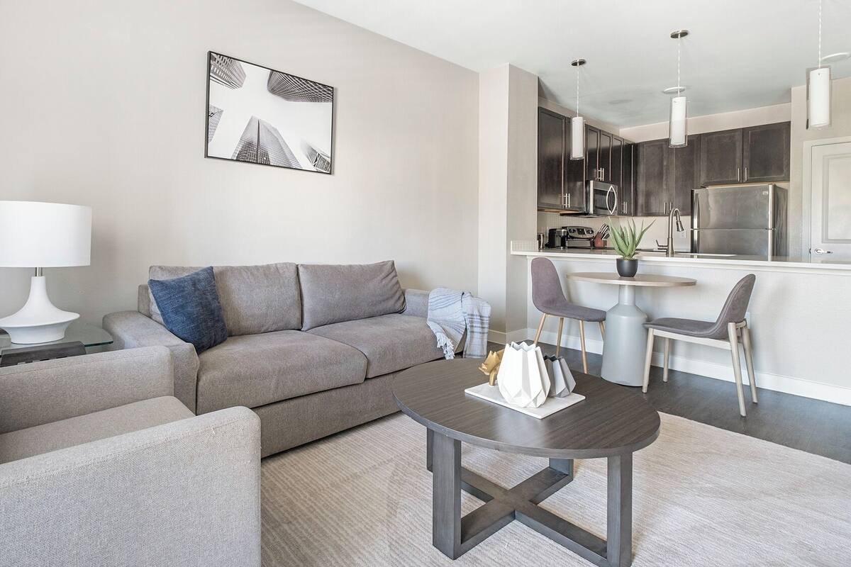 A modern living room with a grey sofa, a coffee table, and a dining area with a small table and chairs.