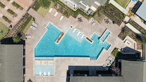 Vue aérienne d’un espace piscine comprenant plusieurs zones, entouré d’un parking et bordé de bâtiments adjacents.