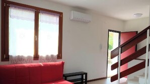 Et værelse med en rød sofa, et lille bord, en trappe og en aircondition.