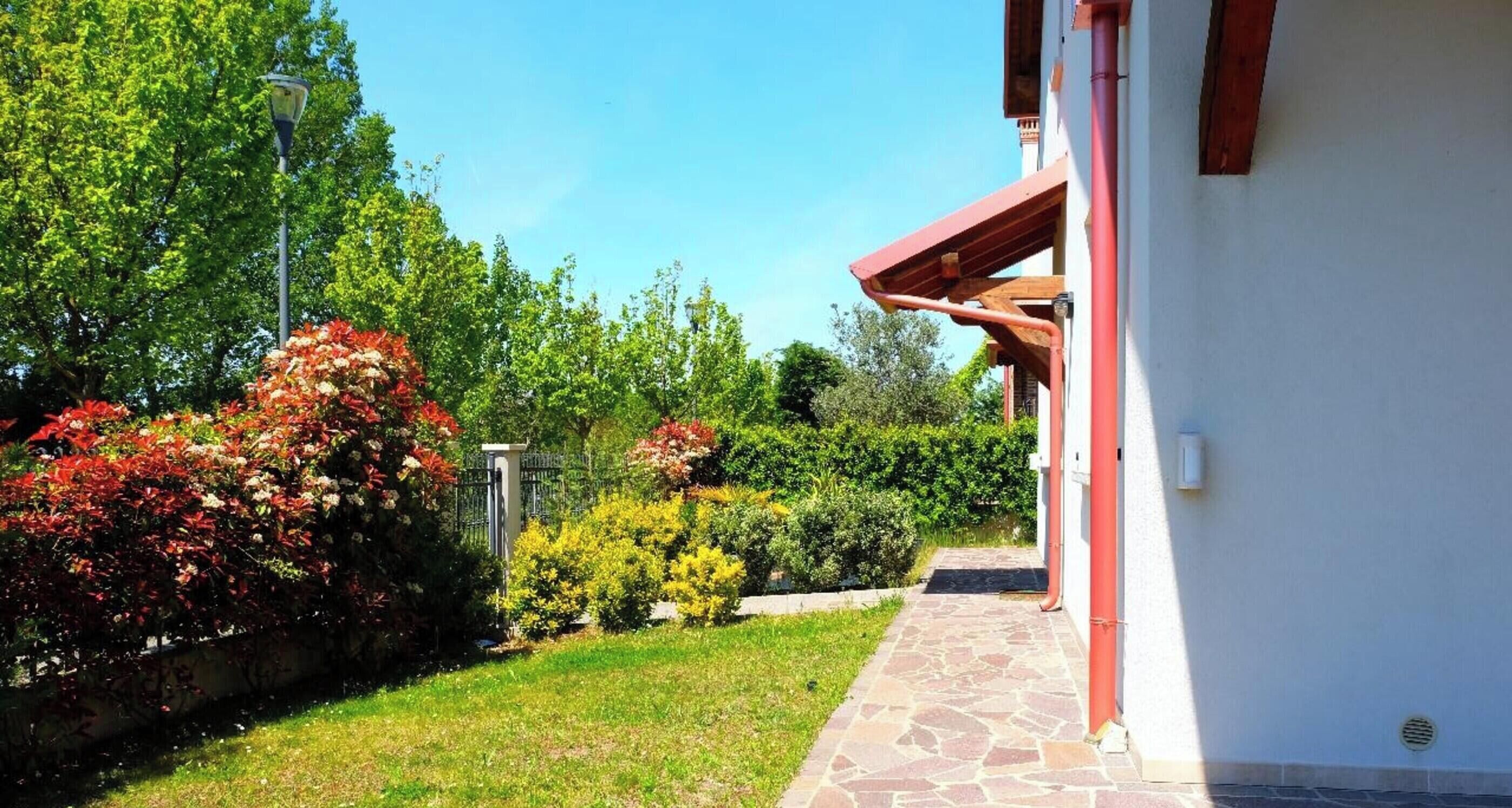Un edificio con un camino de piedra que conduce a una puerta roja, rodeado de abundante vegetación y árboles.