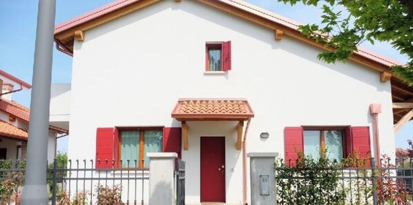 A two-story building with a red door, a small window with a red shutter, and a balcony.
