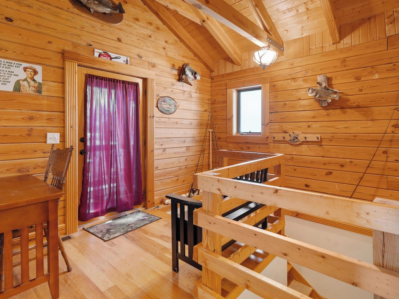 A wooden cabin interior with a dining table, chairs, a window, and a door with a purple curtain.