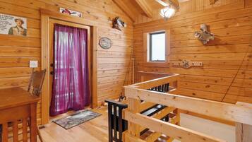 A wooden cabin interior with a dining table, chairs, a window, and a door with a purple curtain.