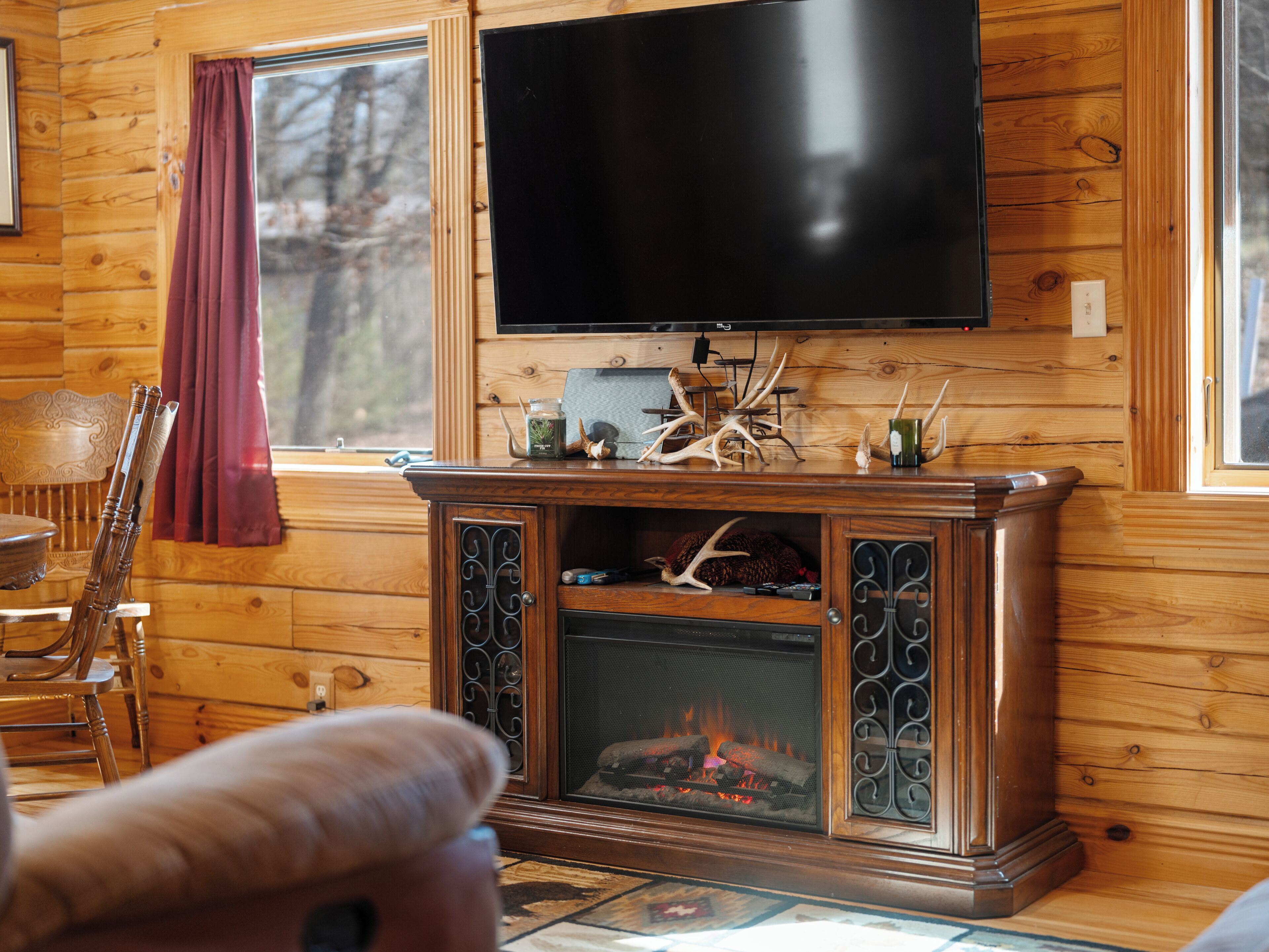 Un interior de madera con chimenea, un televisor montado encima y una zona de comedor con una silla y una mesa.