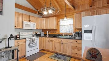 Una cocina con armarios de madera, un refrigerador blanco, un microondas y una lámpara colgante.