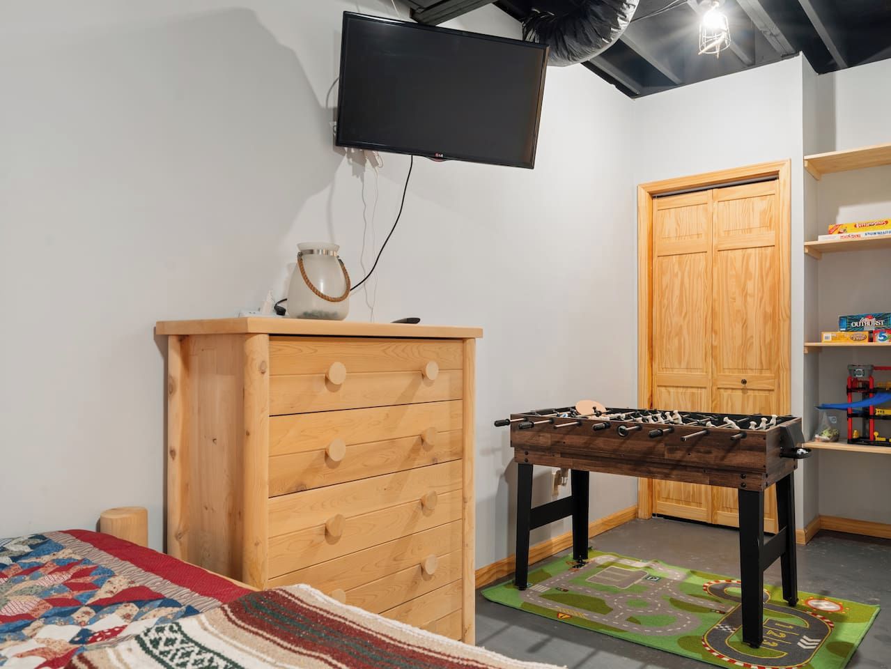 A room with a wooden dresser, a foosball table, a television mounted on the wall, and a wooden door.