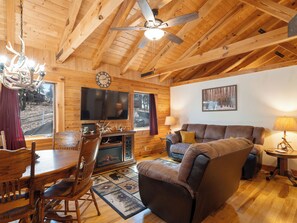 A wooden interior with a ceiling fan, a fireplace, a television, a couch, and a dining area.