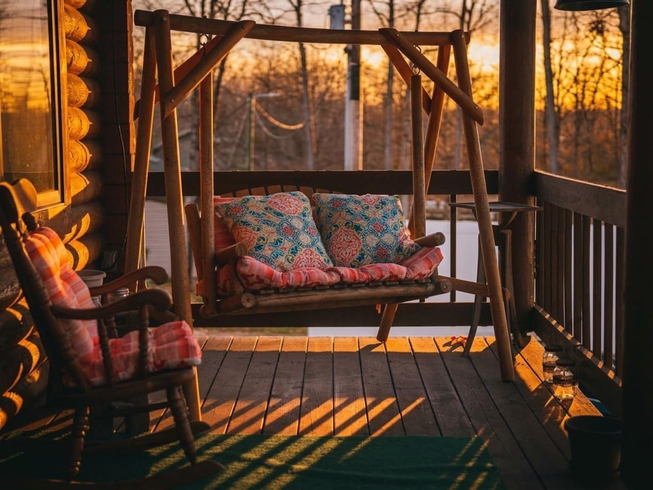 A wooden swing chair and a wooden swing bench with patterned cushions on a porch.